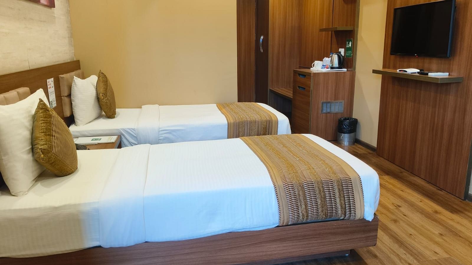 A side view of the room with twin beds, highlighting the room amenities such as an LED TV, wall frame, and a passage leading to the entrance door at Le ROI Digha Hotel, West Bengal.
